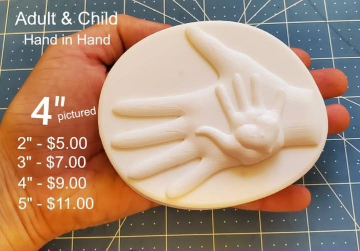 Adult and child hands mold, a small hand resting into an open adult palm on a round disc