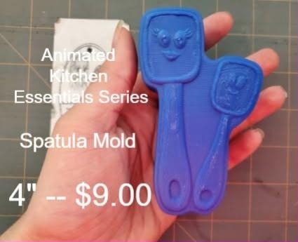 Two cartoon spatula molds with smiling faces and hanging holes, cast in blue