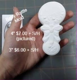 Baby rattle mold with scrollwork across the round head, a bow at the neck and patterned handle