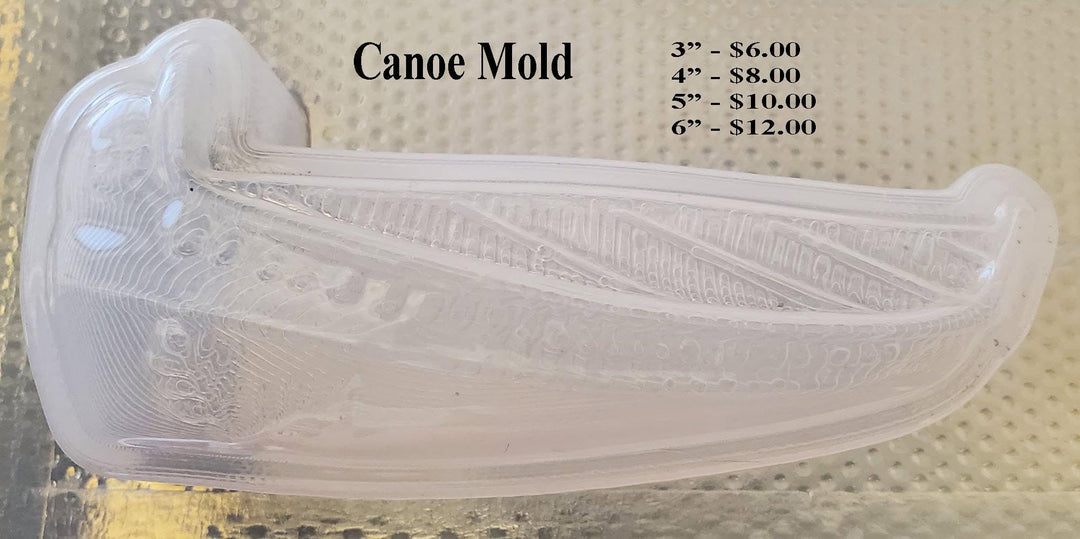 Clear plastic canoe mold on a textured mat, planked hull with diagonal ribbing and a leaf detail at the bow.