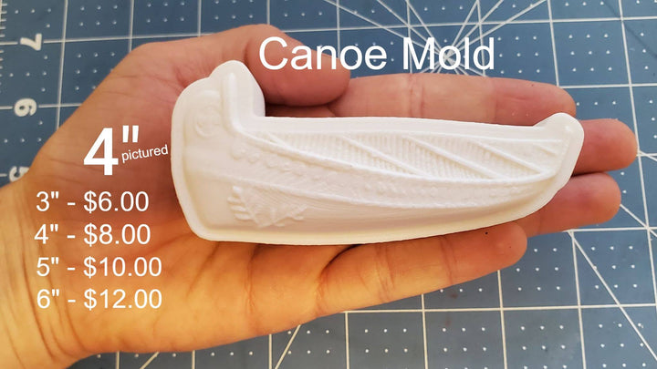 White canoe casting held in a hand, lengthwise planking with diagonal ribs and a leaf motif near the bow.
