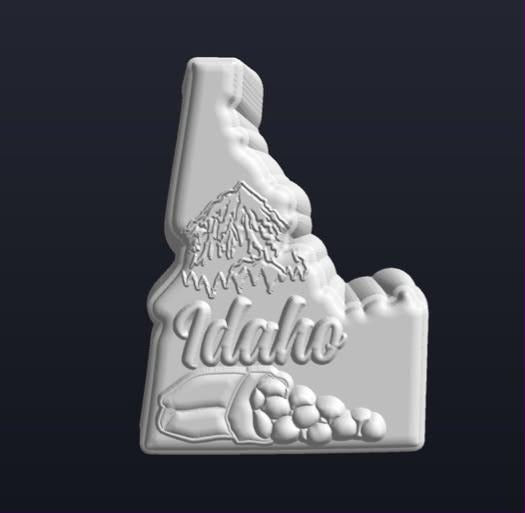 Mold of the Idaho state outline with a mountain, script lettering and potatoes