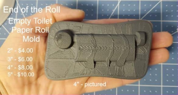 Empty toilet paper roll mold printed in olive plastic, held in a hand, torn paper end visible