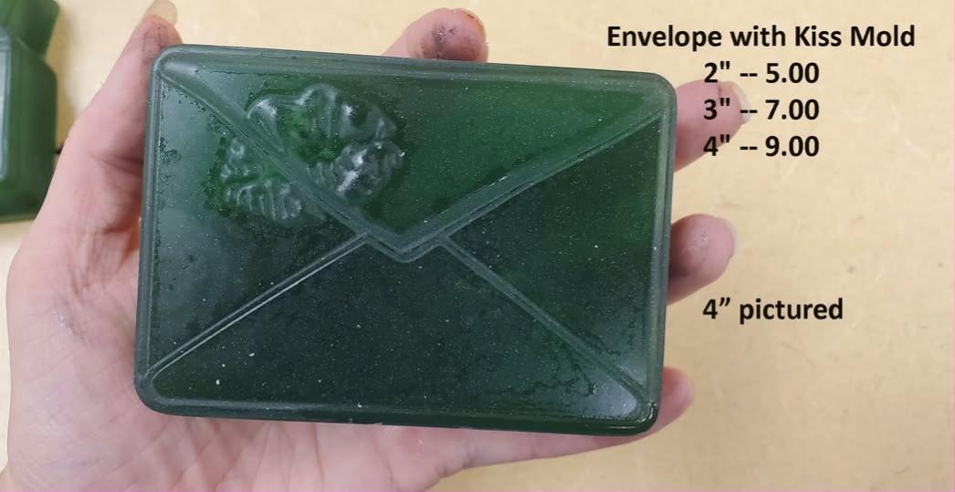 Deep green envelope casting held in a hand, crossed flap seams with a lipstick kiss on the upper flap, shown at the 4 inch size.
