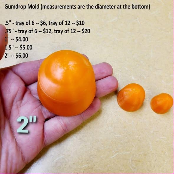 Three orange gumdrop casts in different sizes, smooth domes with flat bottoms, held in a hand