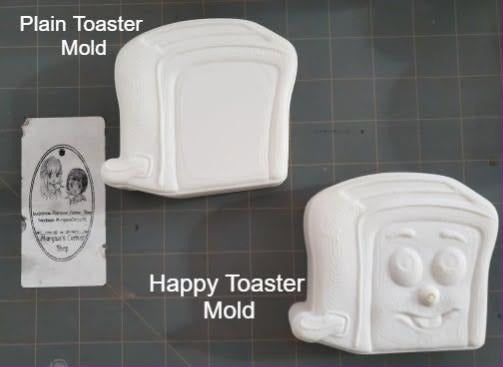 Cast toaster mold with bread slot, side lever and a smiling cartoon face on the front panel