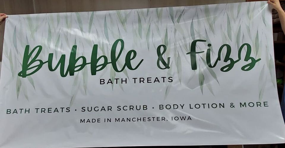 Bubble and Fizz Bath Treats banner held up flat, green script on a white leaf background.