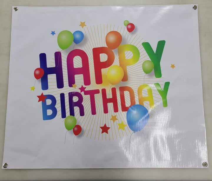White vinyl banner printed HAPPY BIRTHDAY in rainbow letters with balloons and stars.