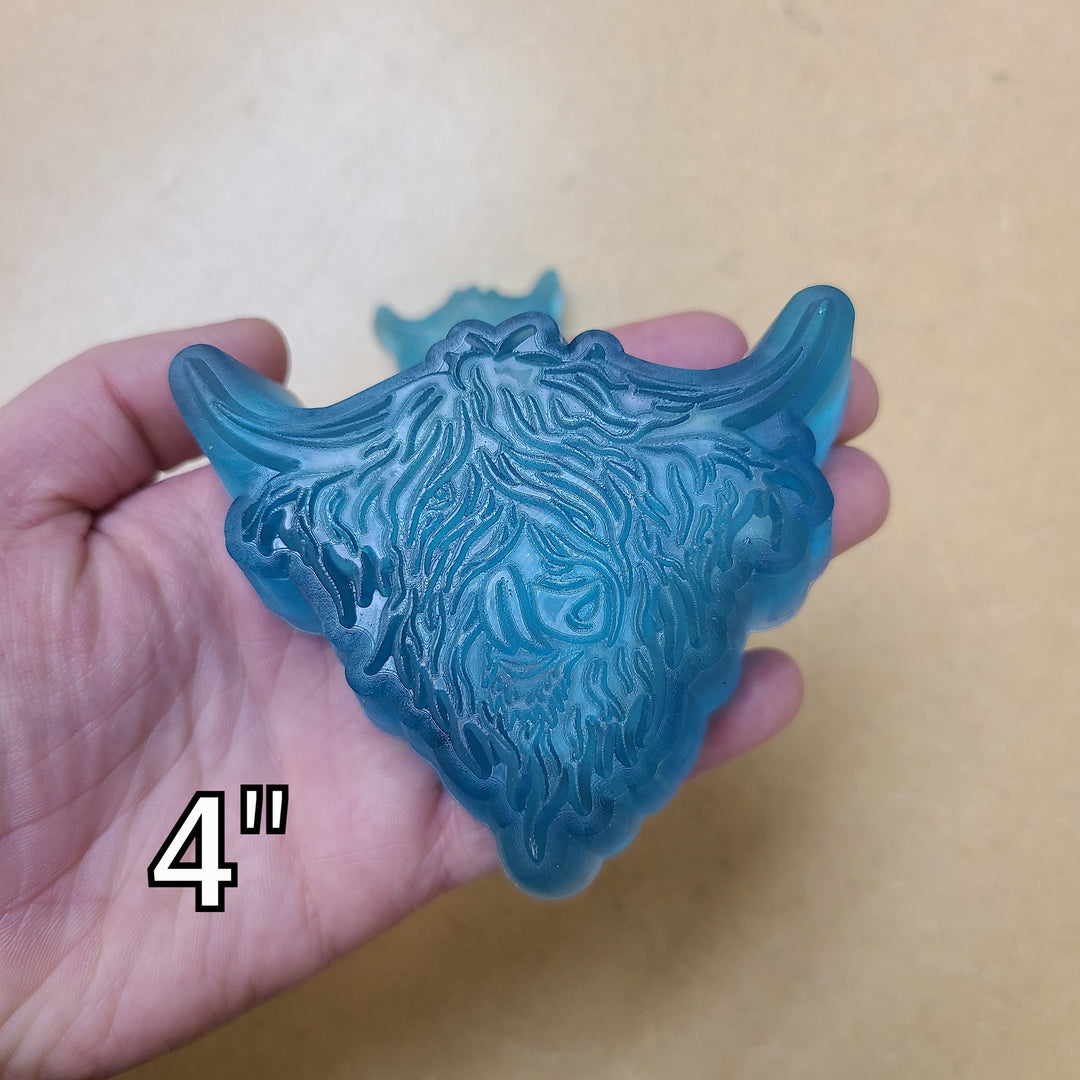 Blue highland cow cast at four inches filling a palm, long fringe and wide upswept horns.