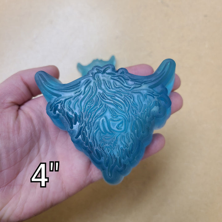 Blue highland cow cast at four inches filling a palm, long fringe and wide upswept horns.