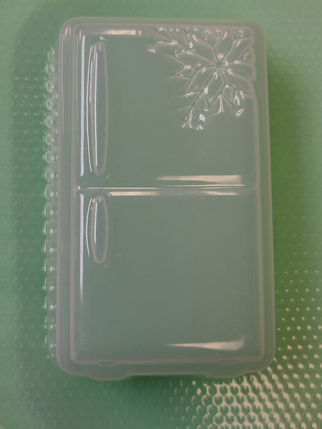Clear plastic refrigerator mold on a green dimpled sheet, freezer door and handles cut in.