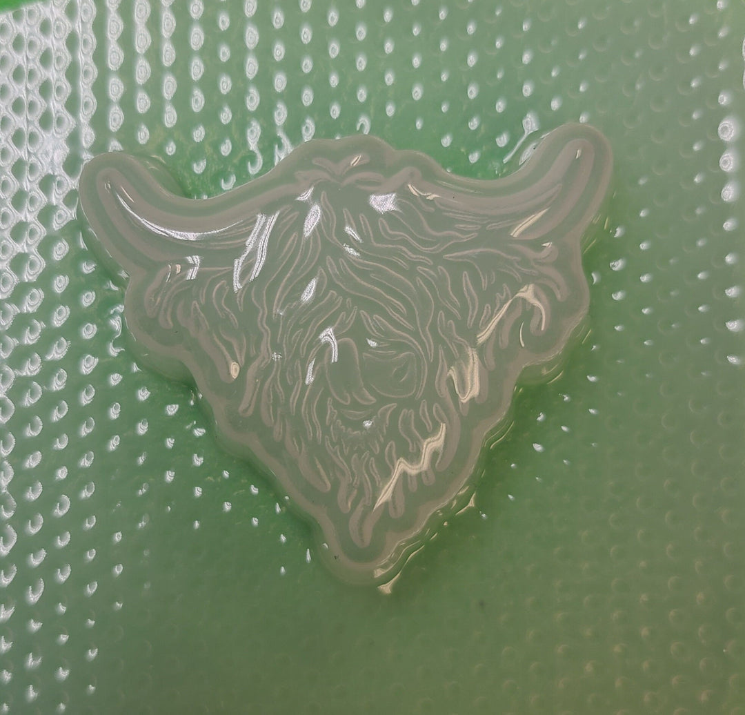 Clear plastic highland cow mold on a green dimpled backing sheet, horns and fringe cut in.
