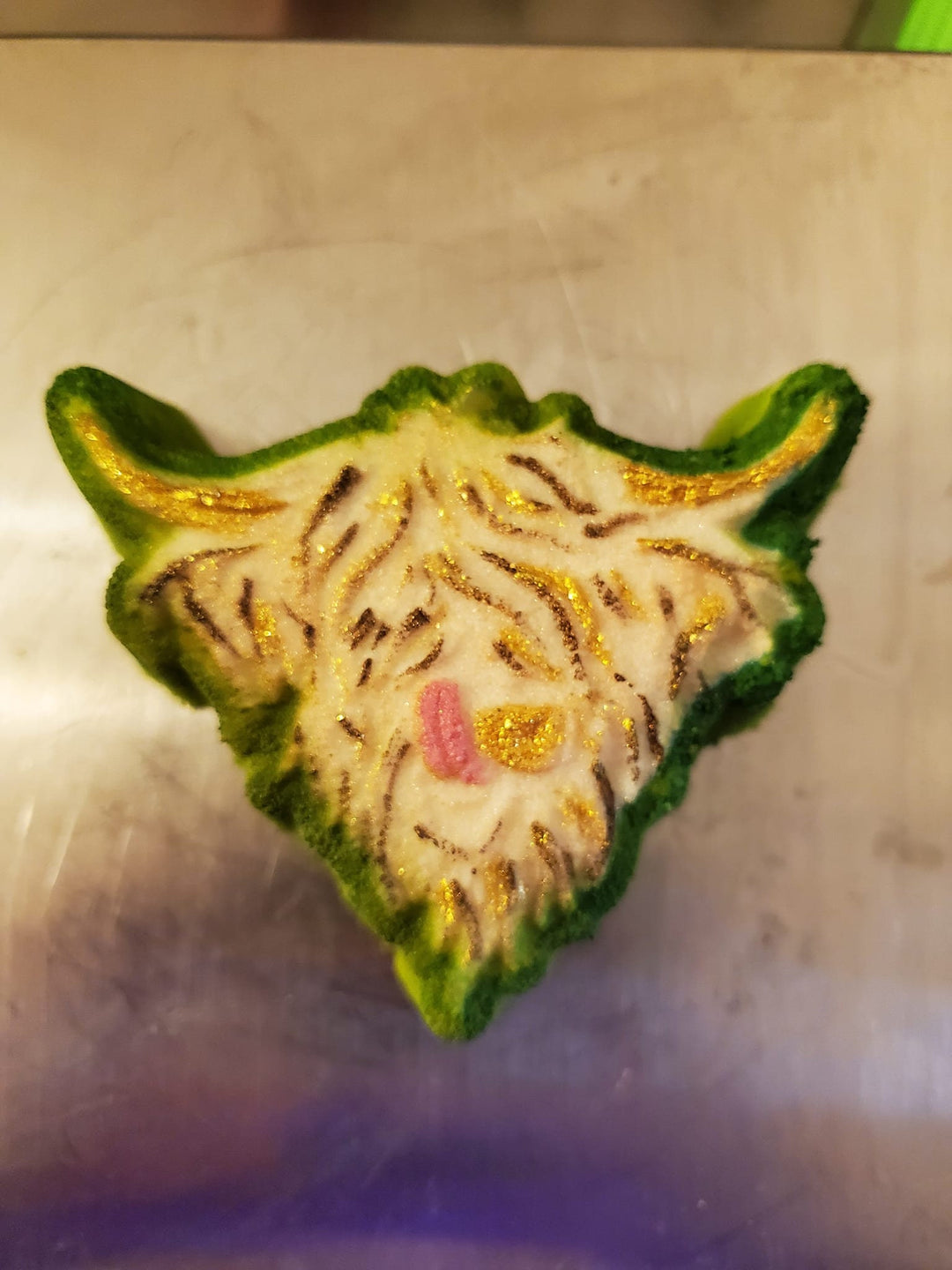 Highland cow head cast painted green and gold with a pink nose, shaggy fringe over the eyes.