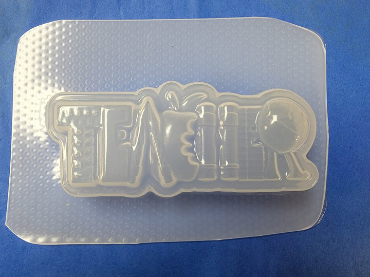 Clear plastic TEACHER mold on a blue mat, ruler, pencil, apple and globe letters cut in.