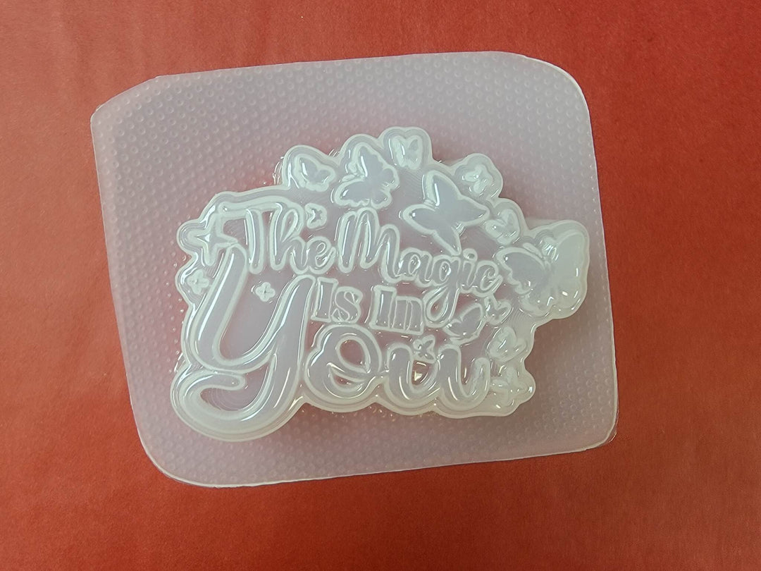 Clear plastic mold of The Magic Is In You plaque with butterflies and sparkles cut in.