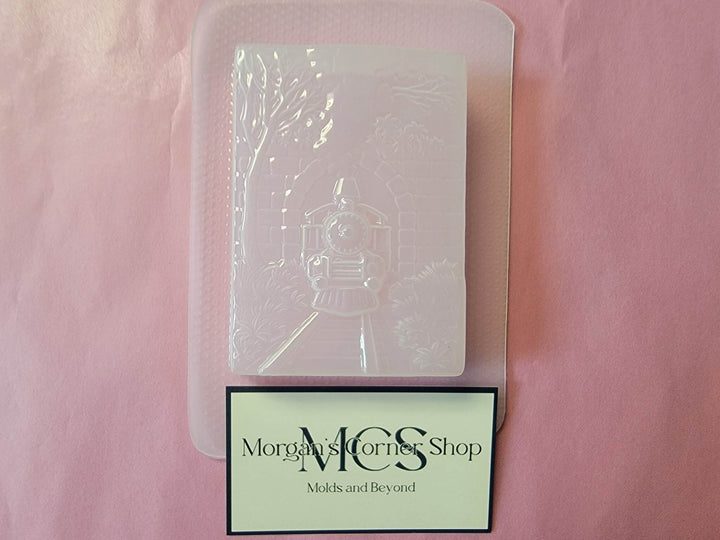 Clear plastic train bridge mold on pink paper beside a Morgan&