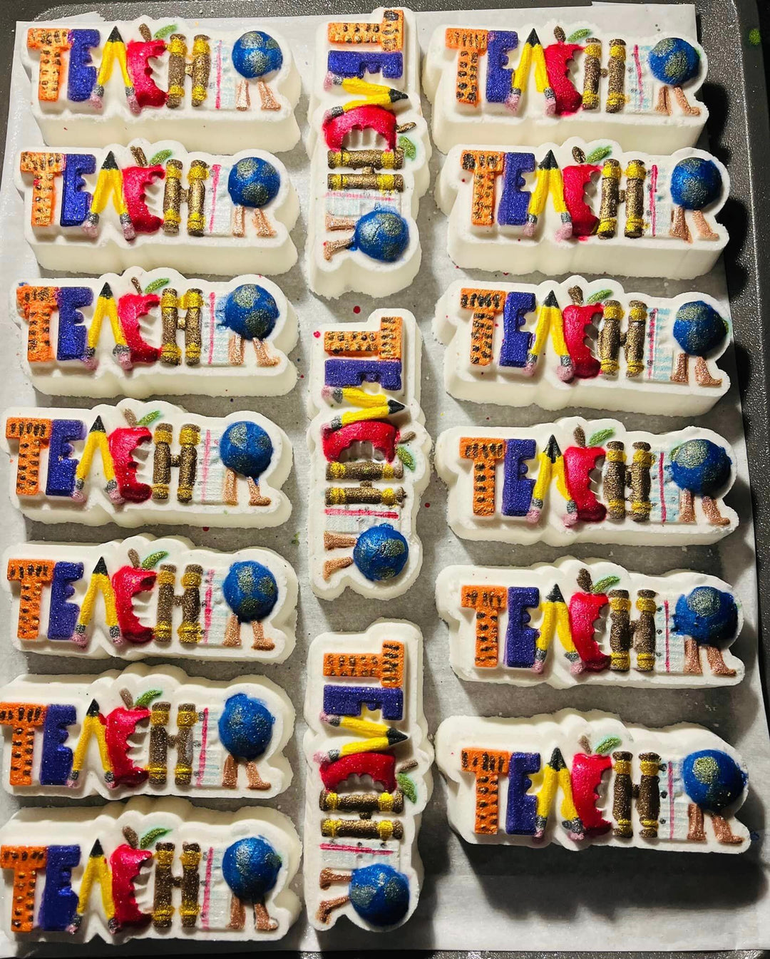 A tray of TEACHER casts lined up in rows, each painted in blues, purples and yellows.