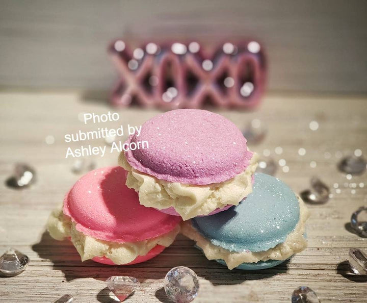 Three macaron bath treats in pink, red and blue with thick cream filling, on wood.