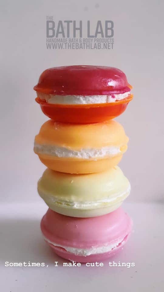 Four macaron soaps stacked in red, orange, cream and pink with cream filling between.
