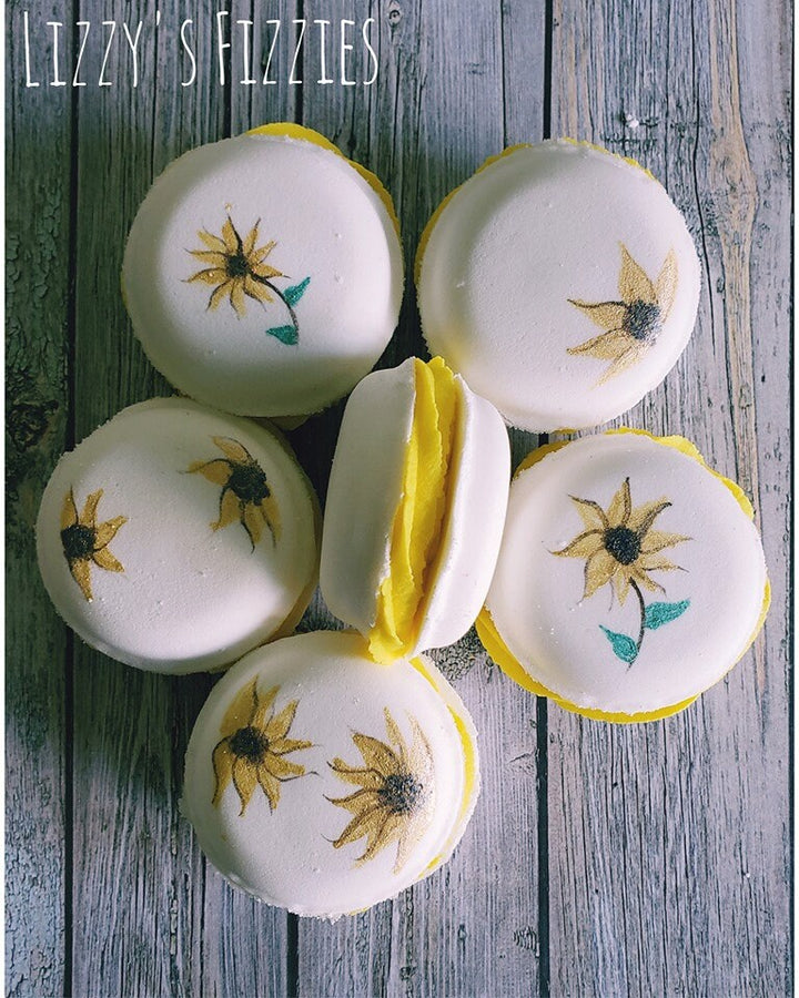Five white macaron casts decorated with sunflowers and a yellow filling strip on boards.