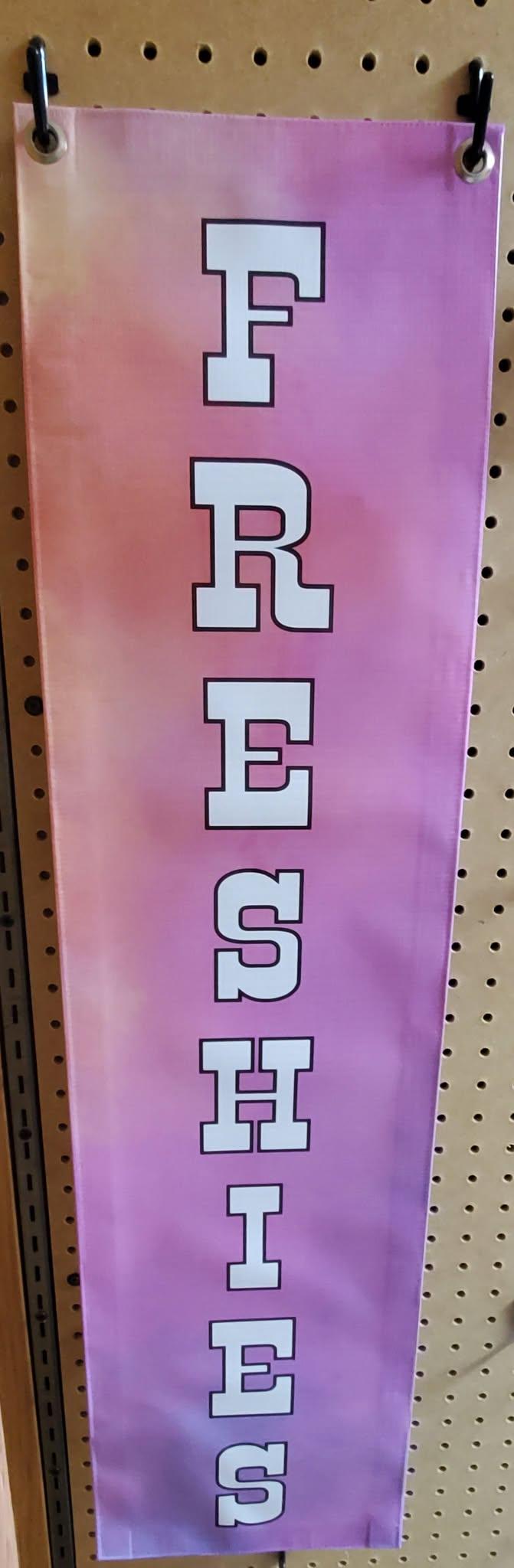 Vertical FRESHIES banner in white letters on pink and purple, hung from a pegboard.