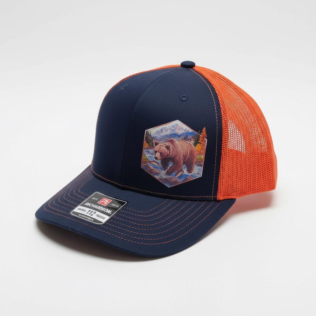 Side view of the navy and orange trucker cap, bear crossing a stream on the patch.