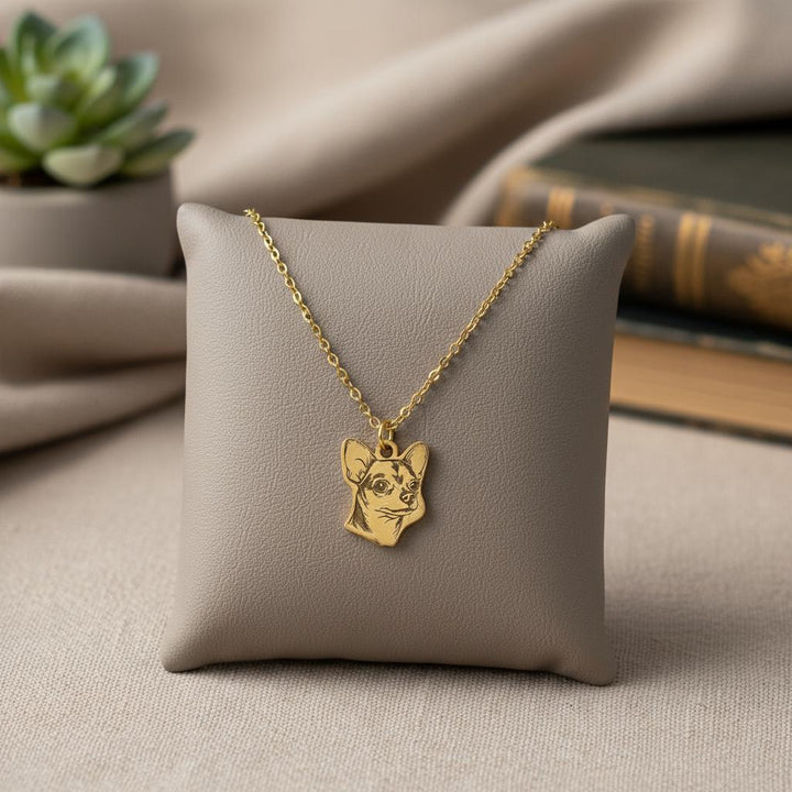 Chihuahua necklace draped over a grey display pillow beside a succulent and books.