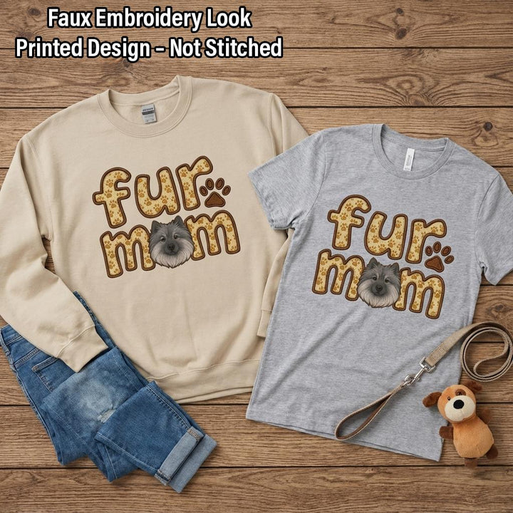Sand sweatshirt and grey tee both printed fur mom with a Keeshond face, laid on wood with jeans.
