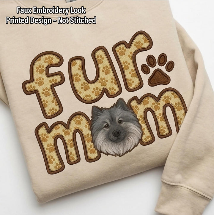 Close view of the fur mom print on sand, letters filled with paw prints around a Keeshond face.