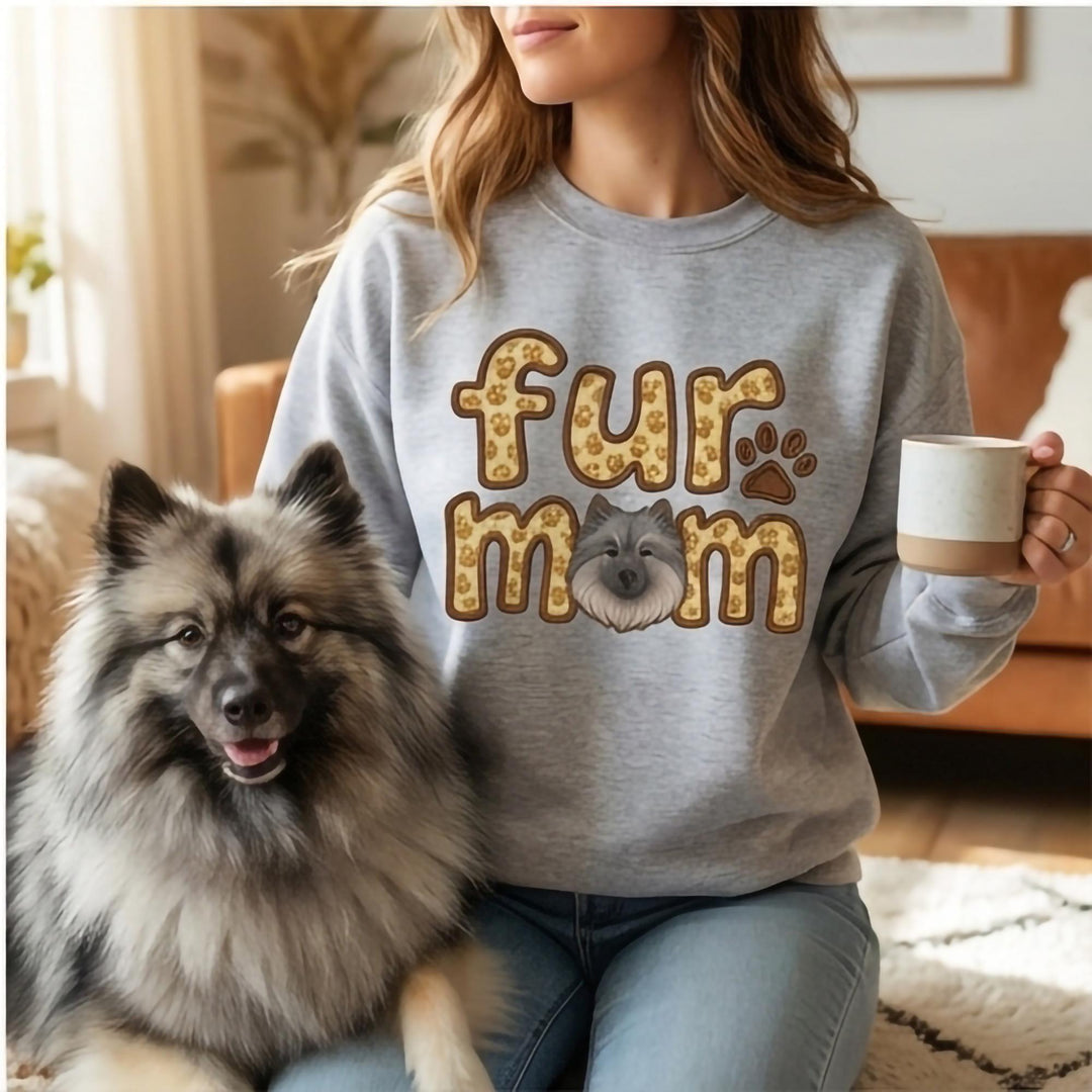 Model in a grey sweatshirt printed fur mom in paw-filled letters with a Keeshond face in the o.