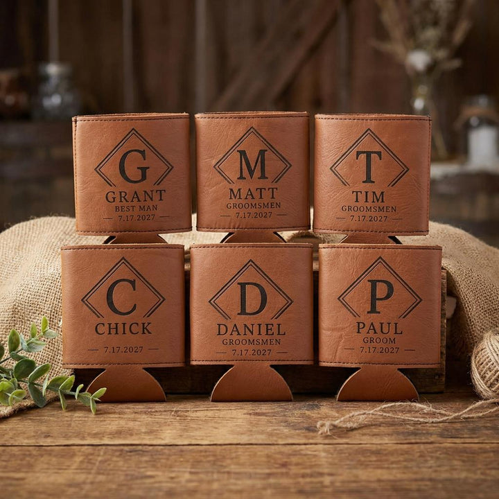 Six engraved leatherette can coolers stacked in two rows on burlap and a rustic bench.