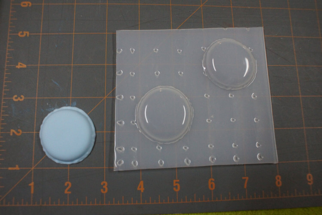 Clear plastic macaron mold with two round shell cavities on a cutting mat for scale.