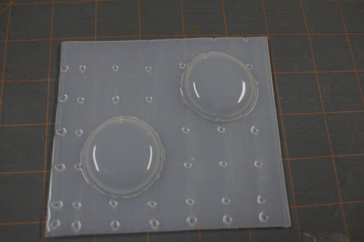 Two-cavity macaron mold on a cutting mat, domed shells about two and a half inches across.