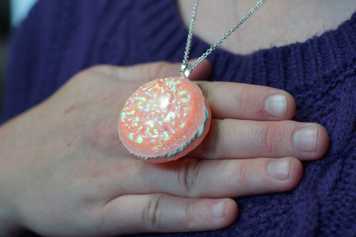 Peach macaron cast with iridescent glitter, drilled and hung as a pendant on a hand.