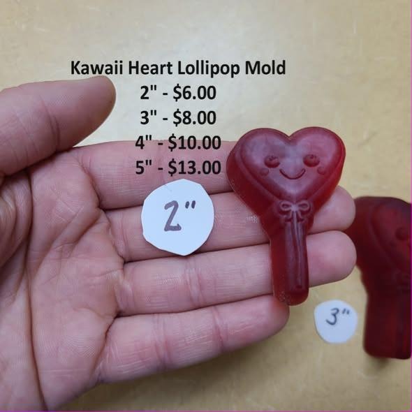 Red cast heart lollipop with a smiling face and a bow at the top of the stick, held in a hand