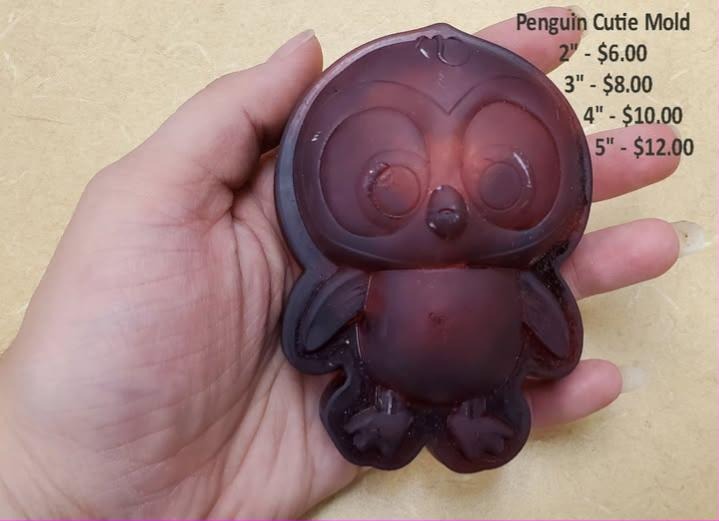 Translucent deep red cast of a chubby baby penguin with big round eyes, held in a hand