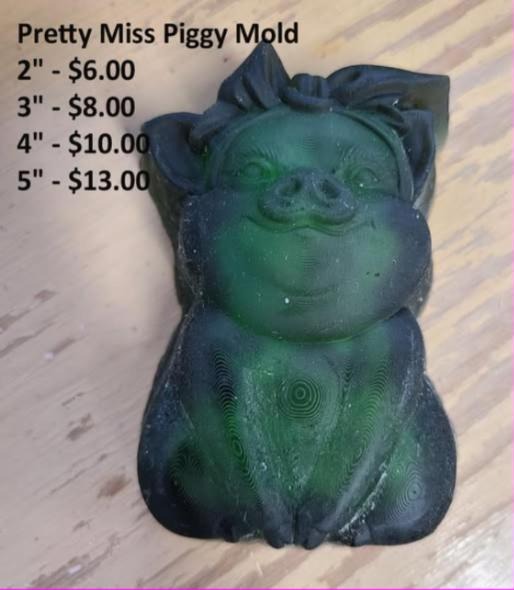 Dark green cast of a seated pig with a bow on her head and trotters folded in front.