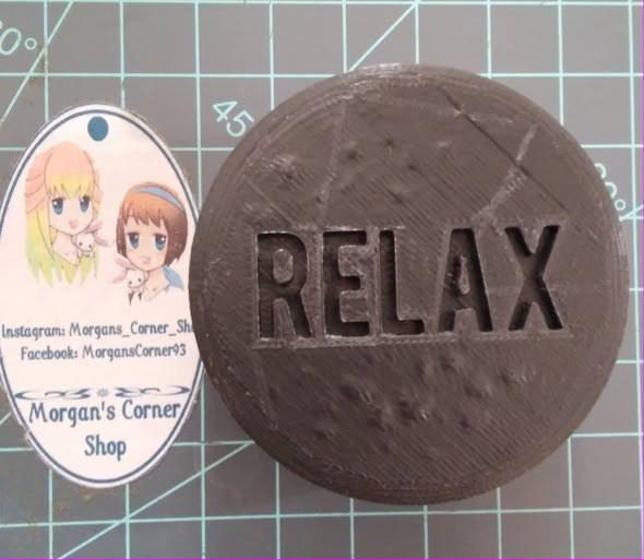 Round shower tablet mold with RELAX in bold block capitals and a lightly dimpled surface.