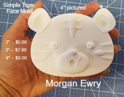 White tiger face cast held in a hand, round ears, striped brow and a wide whiskered muzzle.