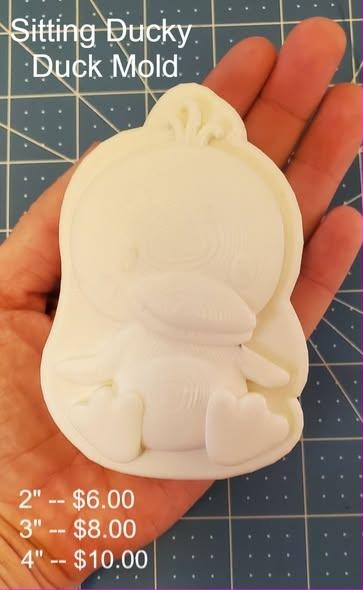 Cream casting of a plump sitting duckling with a folded wing and a short rounded bill, held in a hand