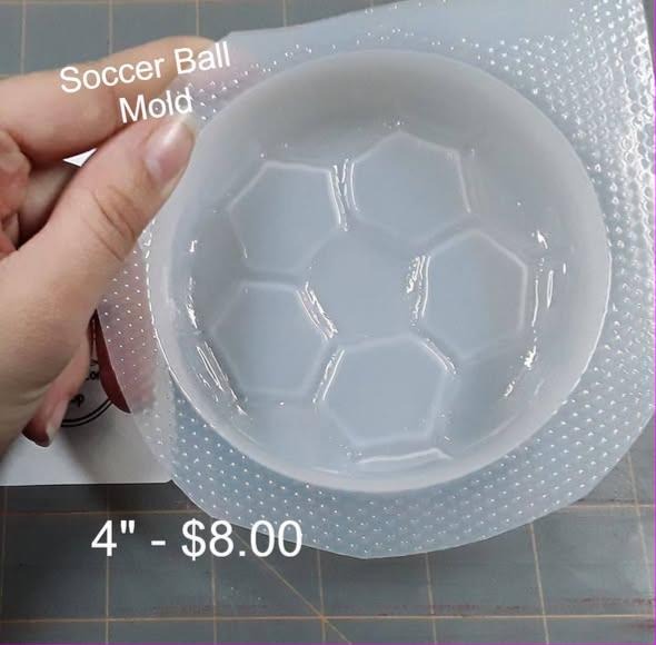 Clear plastic domed soccer ball mold with hexagon and pentagon panels, held in a hand