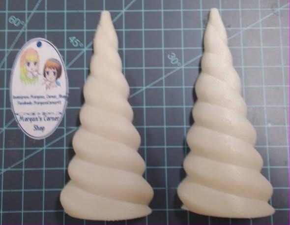 Two cream cast unicorn horn halves with deep spiral twists, standing on a cutting mat.
