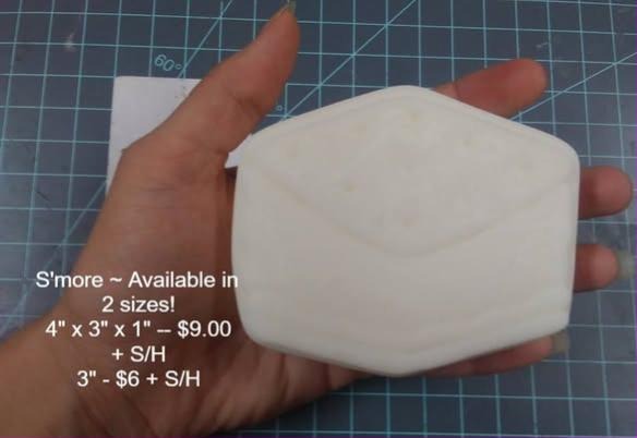 Plain white s'more mold blank held in a palm, a thick six-sided slab with a peaked top.